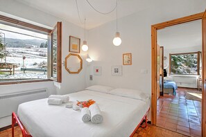 Een hotelkamer met een bed, een raam met uitzicht op een besneeuwd landschap en een badkamer zichtbaar door een geopende deur.