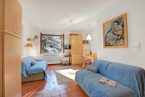 Een gezellige woonkamer met twee banken, een eethoek met een tafel en stoelen, een keuken met een magnetron en waterkoker, en een groot raam met uitzicht op met sneeuw bedekte bomen.