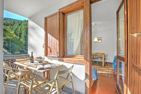 A wooden-framed balcony with a table, chairs, and a bottle of wine.