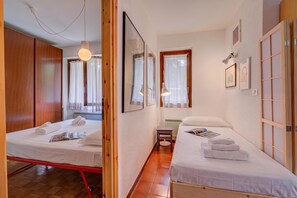 A hotel room with two beds, a wooden wardrobe, a small table, and a window with curtains.