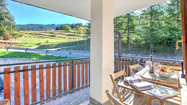 Un balcon avec une table dressée pour le dîner, une chaise et une vue sur une route et des collines.