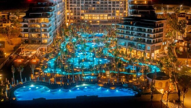 Ein großes Hotel mit mehreren Etagen, einem zentralen Pool und umliegenden Palmen.