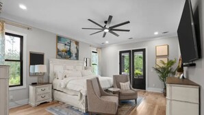 Une chambre à coucher comprenant un lit, deux chaises, une table de chevet, une commode et un ventilateur de plafond.