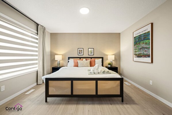Een moderne hotelkamer met een groot bed, twee nachtkastjes met lampen, een ingelijste afbeelding aan de muur en een raam met zonwering.