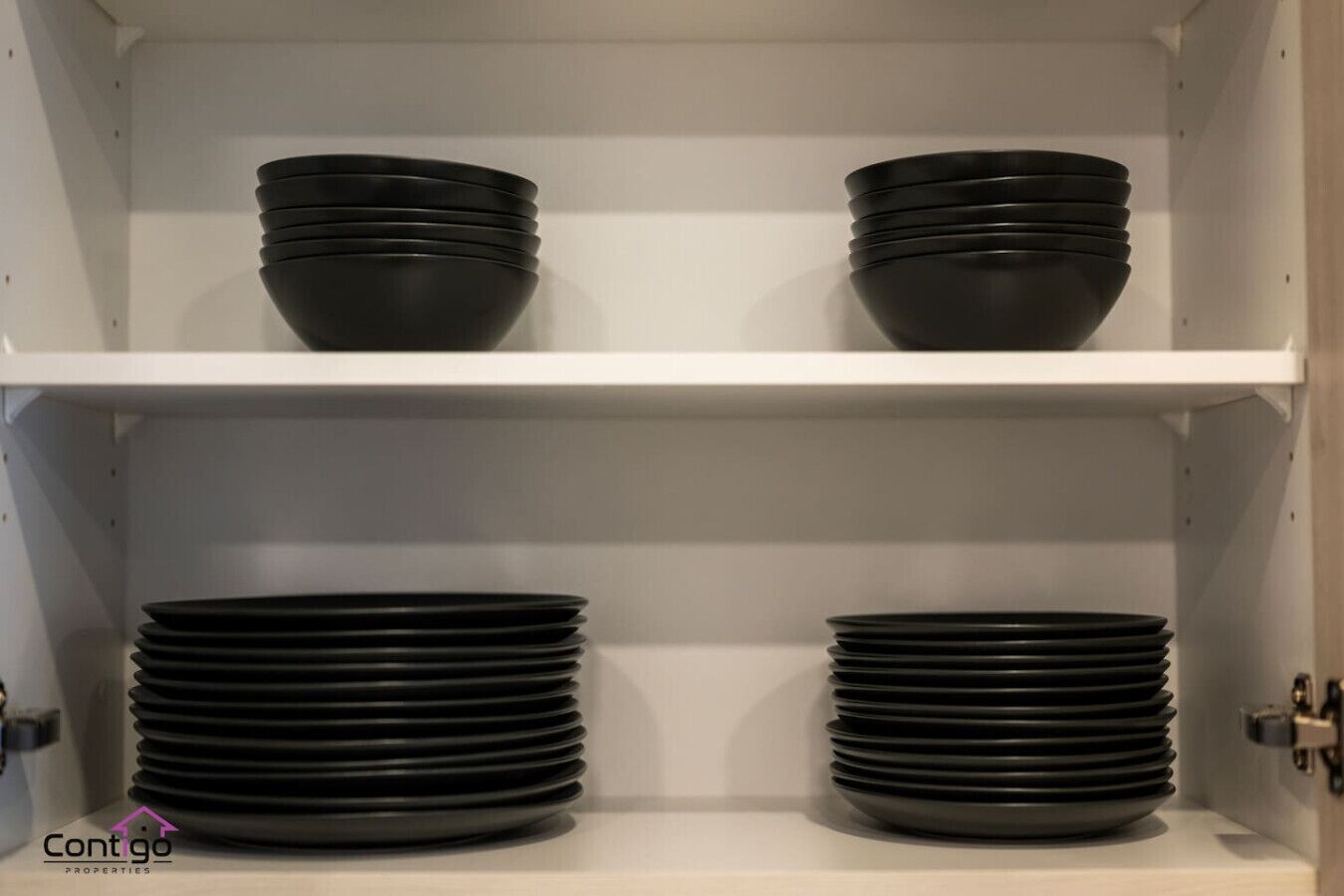 A white shelving unit with black bowls and plates stacked on it.
