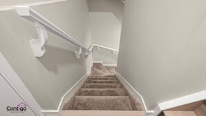Una scala con gradini rivestiti di moquette e corrimano bianchi, che conduce a un piano superiore.