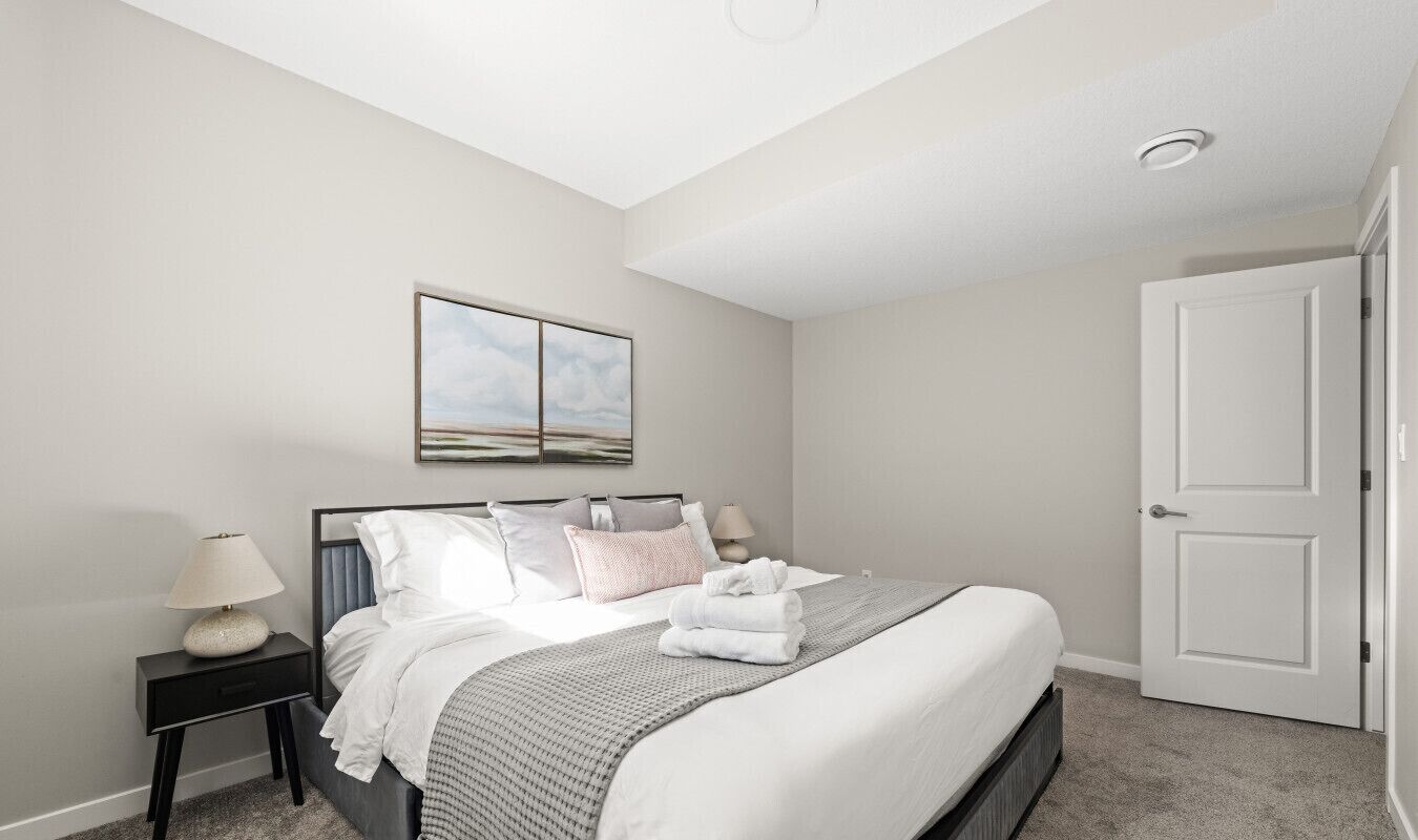 A bedroom with a bed, a nightstand, a lamp, a door, and a wall-mounted picture.