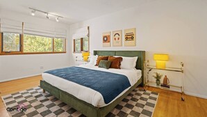 Een moderne slaapkamer met een groot bed, een geruit vloerkleed en een raam met uitzicht op bomen.