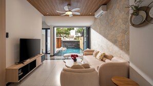 Una sala de estar moderna con televisor de pantalla plana, ventilador de techo, pared de piedra, sofá y una mesita con un florero.