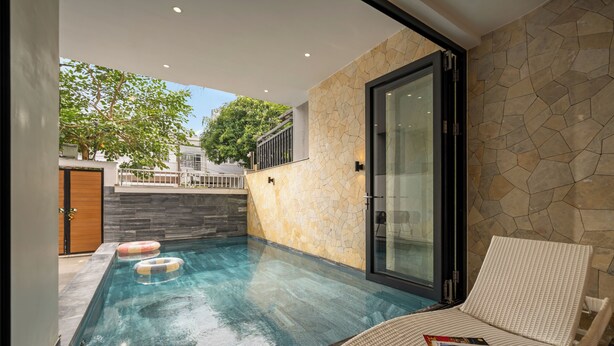 Una piscina interior moderna con agua cristalina, una puerta de vidrio y una silla de descanso con una revista.