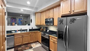 A modern kitchen with wooden cabinets, stainless steel appliances, and a patterned rug. - The Grand Red Quill.  3-bedroom house in Winter Park (Winter Park)