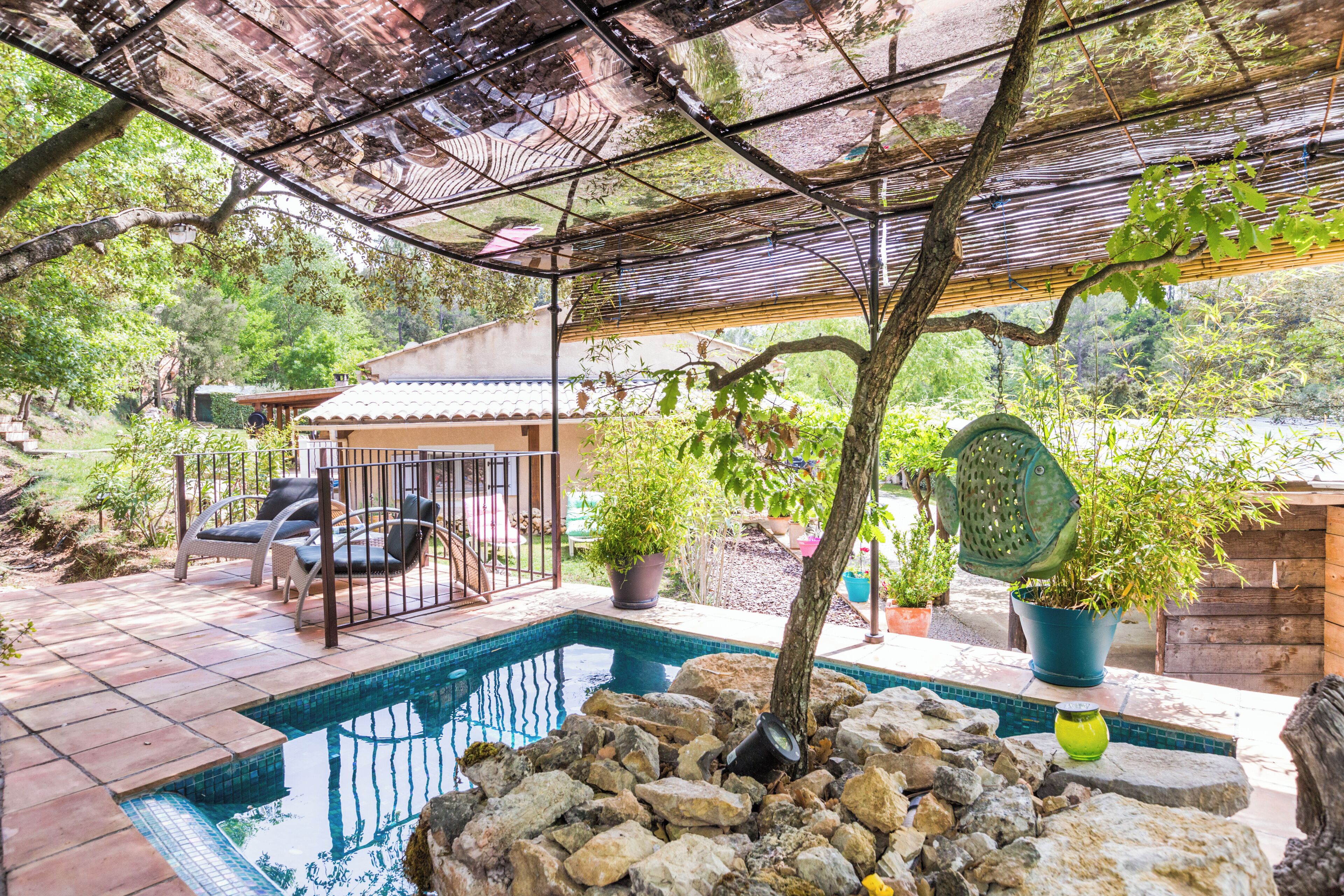 A swimming pool surrounded by rocks, with a covered patio area and potted plants.