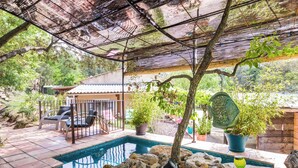 A swimming pool surrounded by rocks, with a covered patio area and potted plants. - Villa with Independent Studio, Pool, Jacuzzi, Playground, Quiet Nature (CHATEAUVERT)