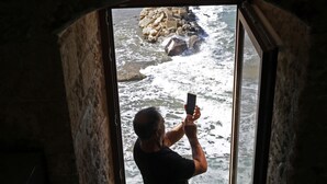 Eine Person fotografiert eine felsige Küstenlinie durch einen Durchgang.