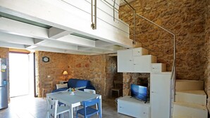 Ein geräumiger Wohnbereich mit Steinwand, einem blauen Sofa, einem Esstisch mit Stühlen, einem Fernseher und einer Treppe.