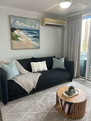 Ein Wohnzimmer mit einem schwarzen Sofa, einer weißen Decke und einem runden Couchtisch mit einer Pflanze.
