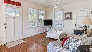 Un salon avec un canapé blanc, une table basse, un téléviseur et un ventilateur de plafond.