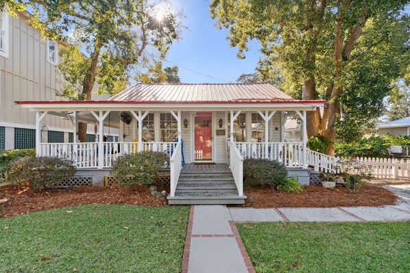 A two-story house with a porch, a red door, and a small front yard with a pathway leading to the entrance.