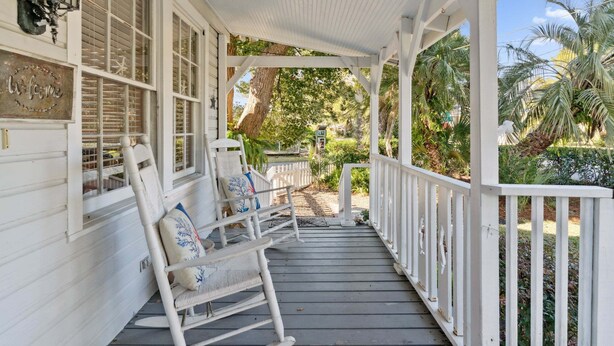 Une véranda couverte avec des balustrades blanches, une chaise berçante et une pancarte indiquant « Bienvenue ».