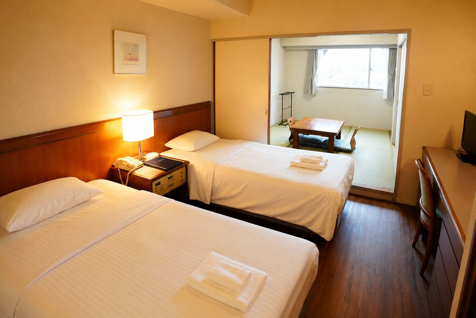 Habitación de hotel con dos camas, un escritorio, una silla, un televisor y una ventana con cortinas.
