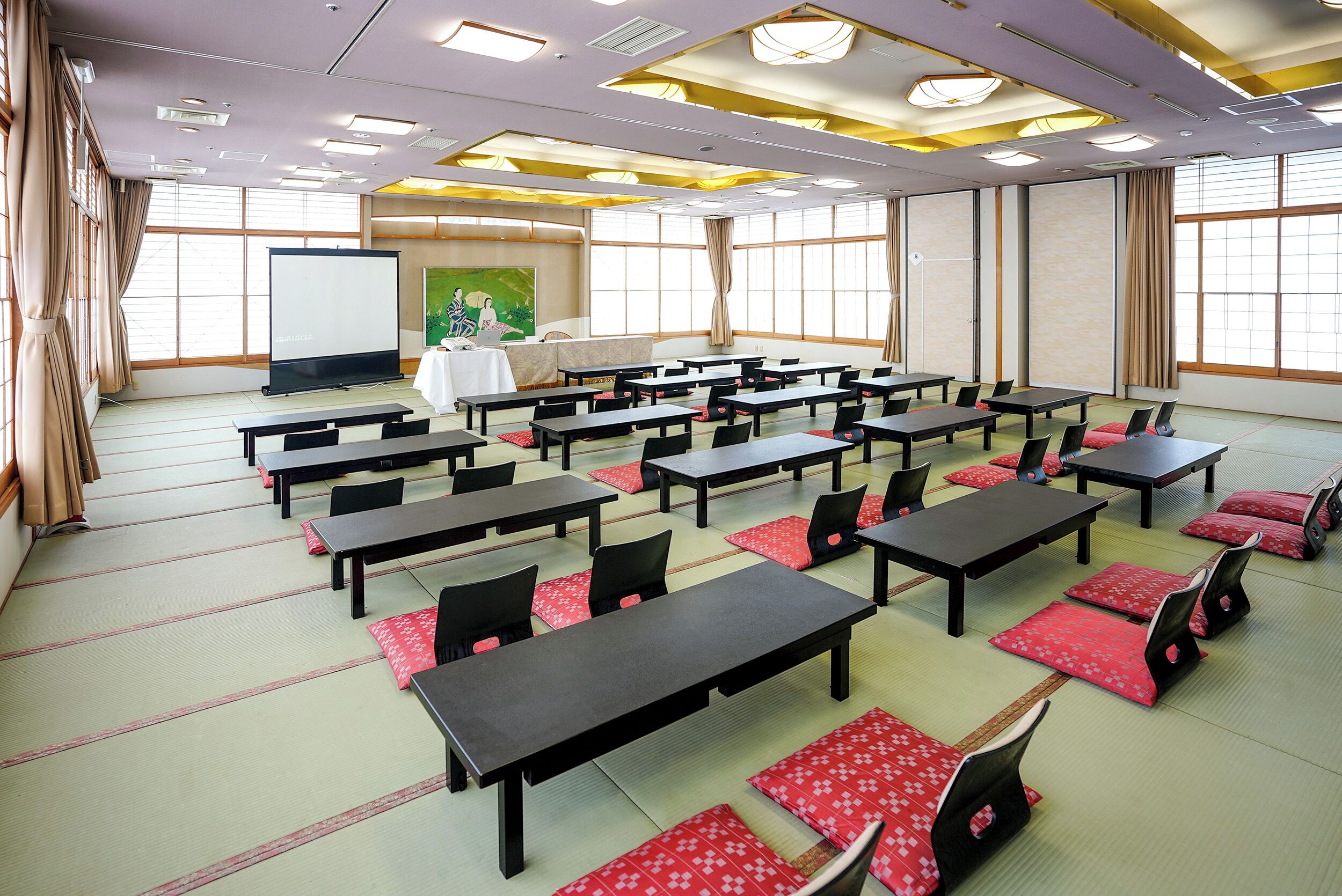 A conference room with tables and chairs, a projector screen, and a painting on the wall.