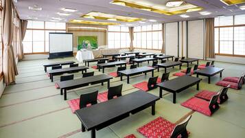 A conference room with tables and chairs, a projector screen, and a painting on the wall.