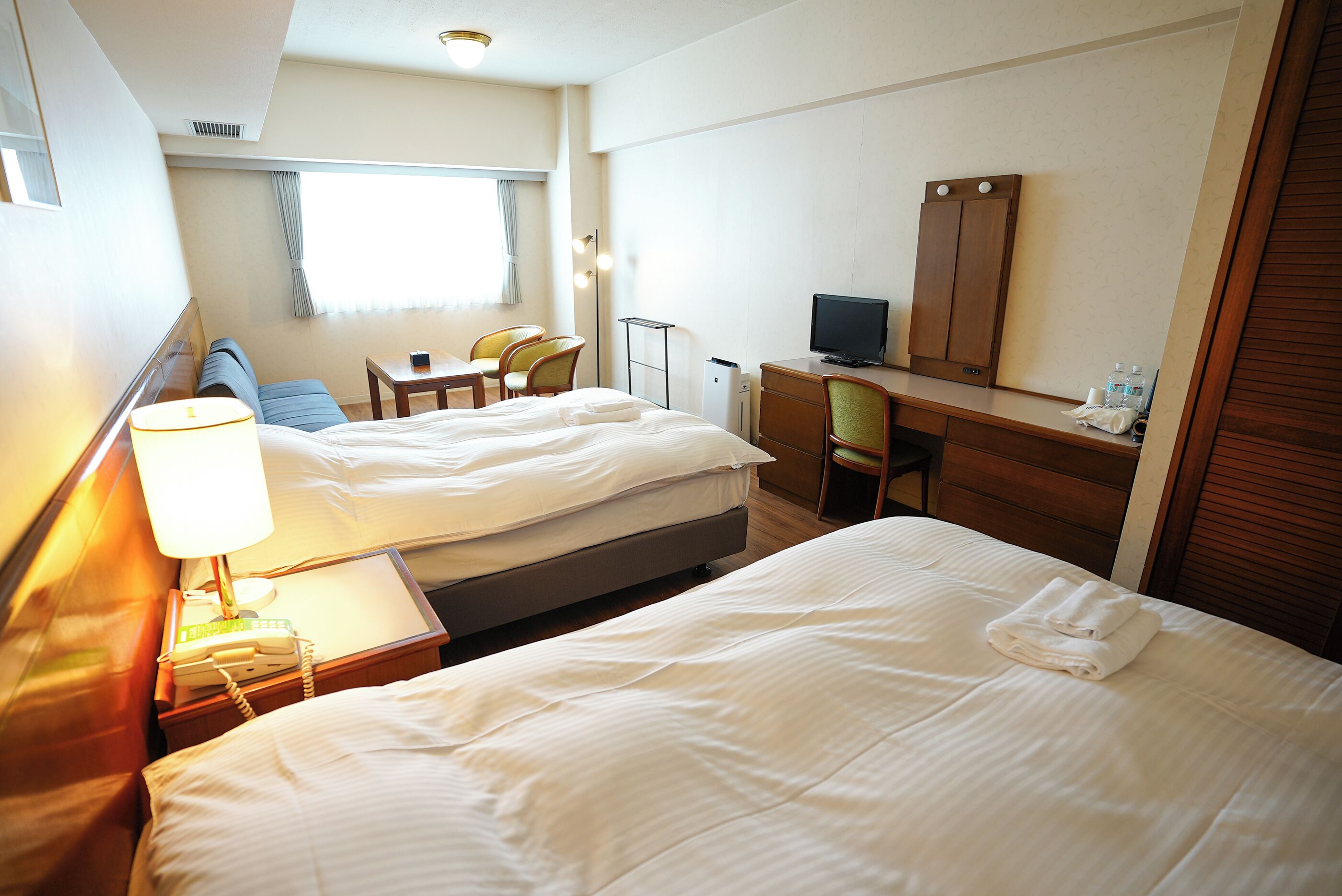 A hotel room with two beds, a desk, a chair, a television, and a wardrobe.