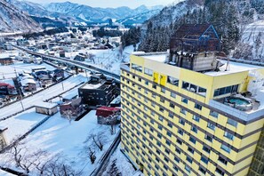Un edificio moderno con numerosi piani, una piscina sul tetto e vista su una cittadina innevata.