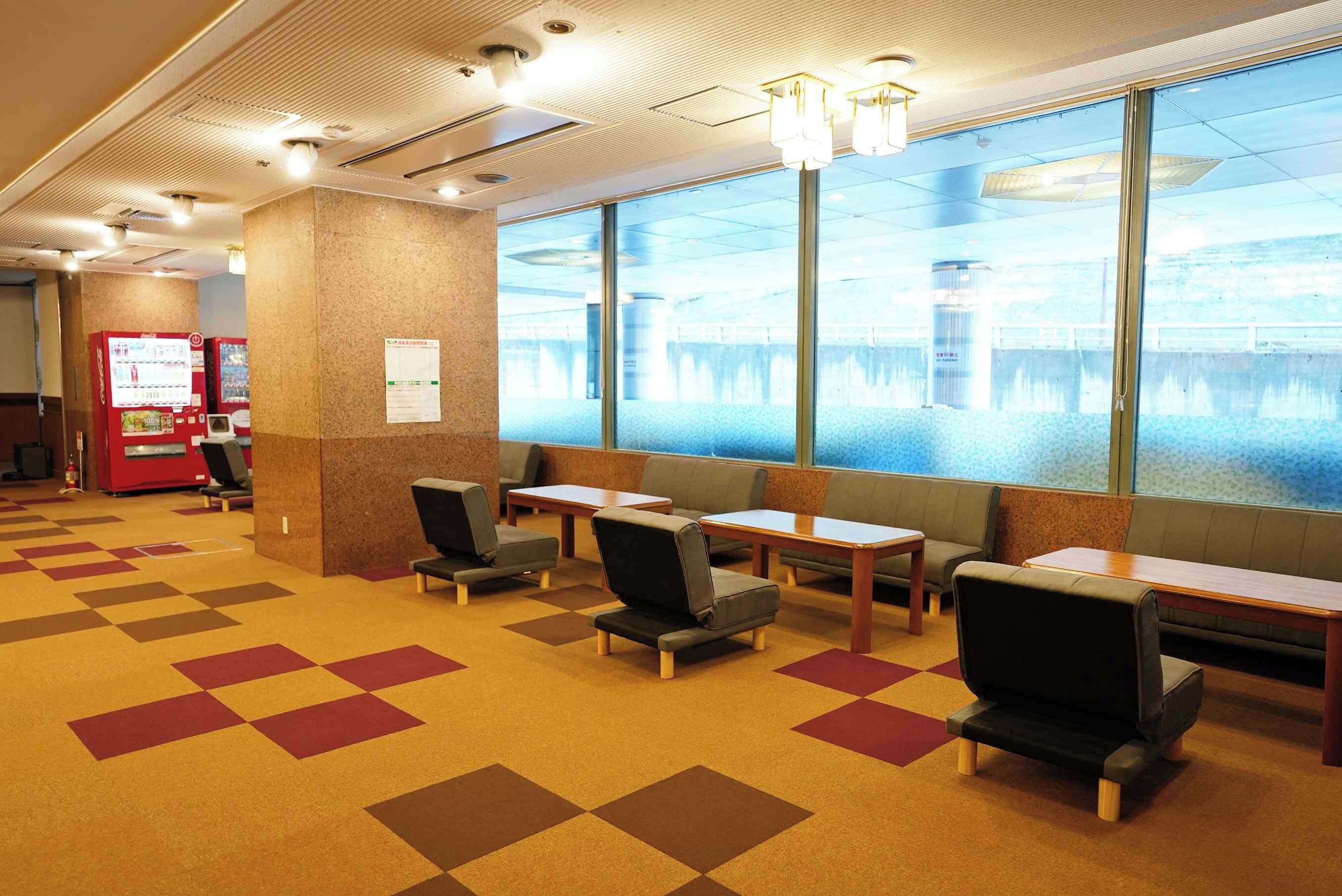 A hotel lobby with seating areas, vending machines, and a view of a body of water through large windows.