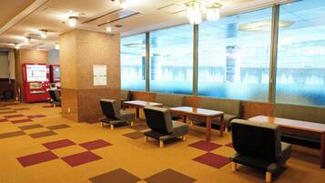 A hotel lobby with seating areas, vending machines, and a view of a body of water through large windows.