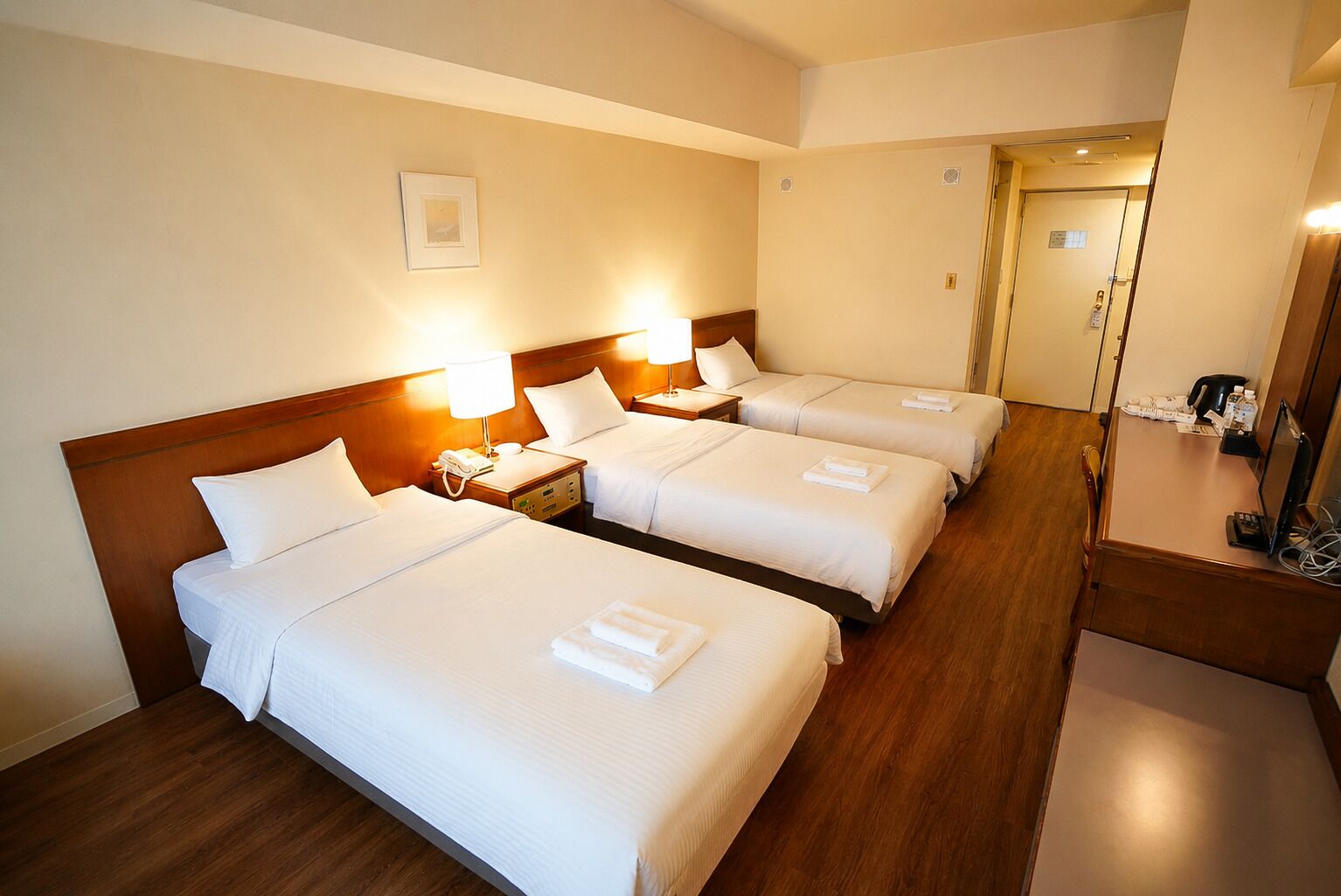 Une chambre d’hôtel avec trois lits, un bureau, une chaise et un miroir.