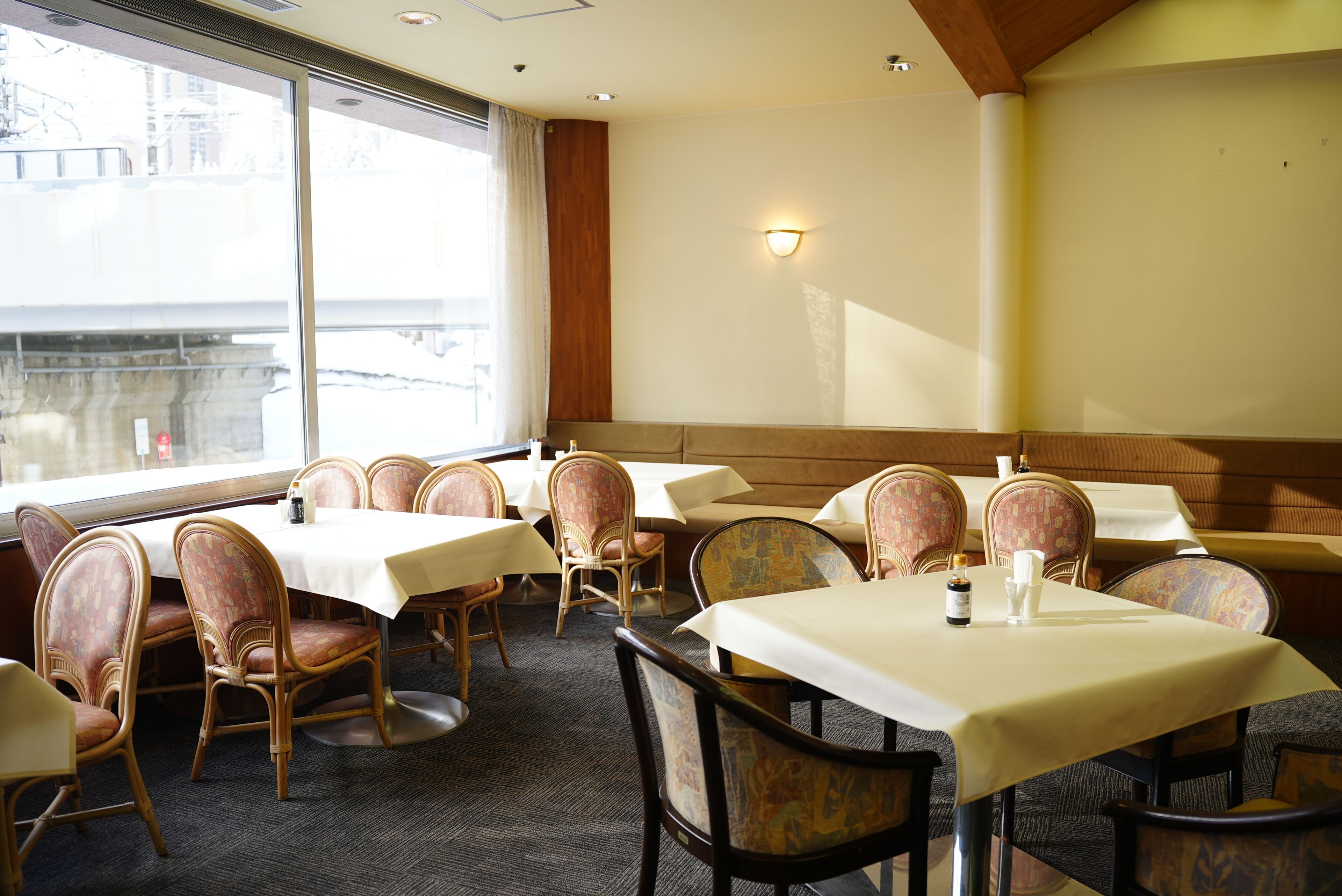 A restaurant with tables and chairs, a window with a view, and a wall-mounted light fixture.