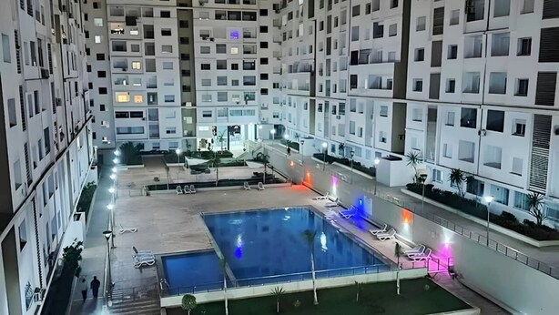 Ett modernt bostadskomplex med flera höga byggnader, en central innergård med en swimmingpool och utomhusområden med sittplatser.