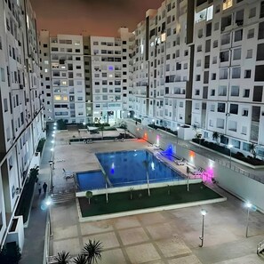 Un complexe d’appartements moderne composé de plusieurs immeubles de grande hauteur, avec une cour intérieure dotée d’une piscine et des espaces de détente en plein air.