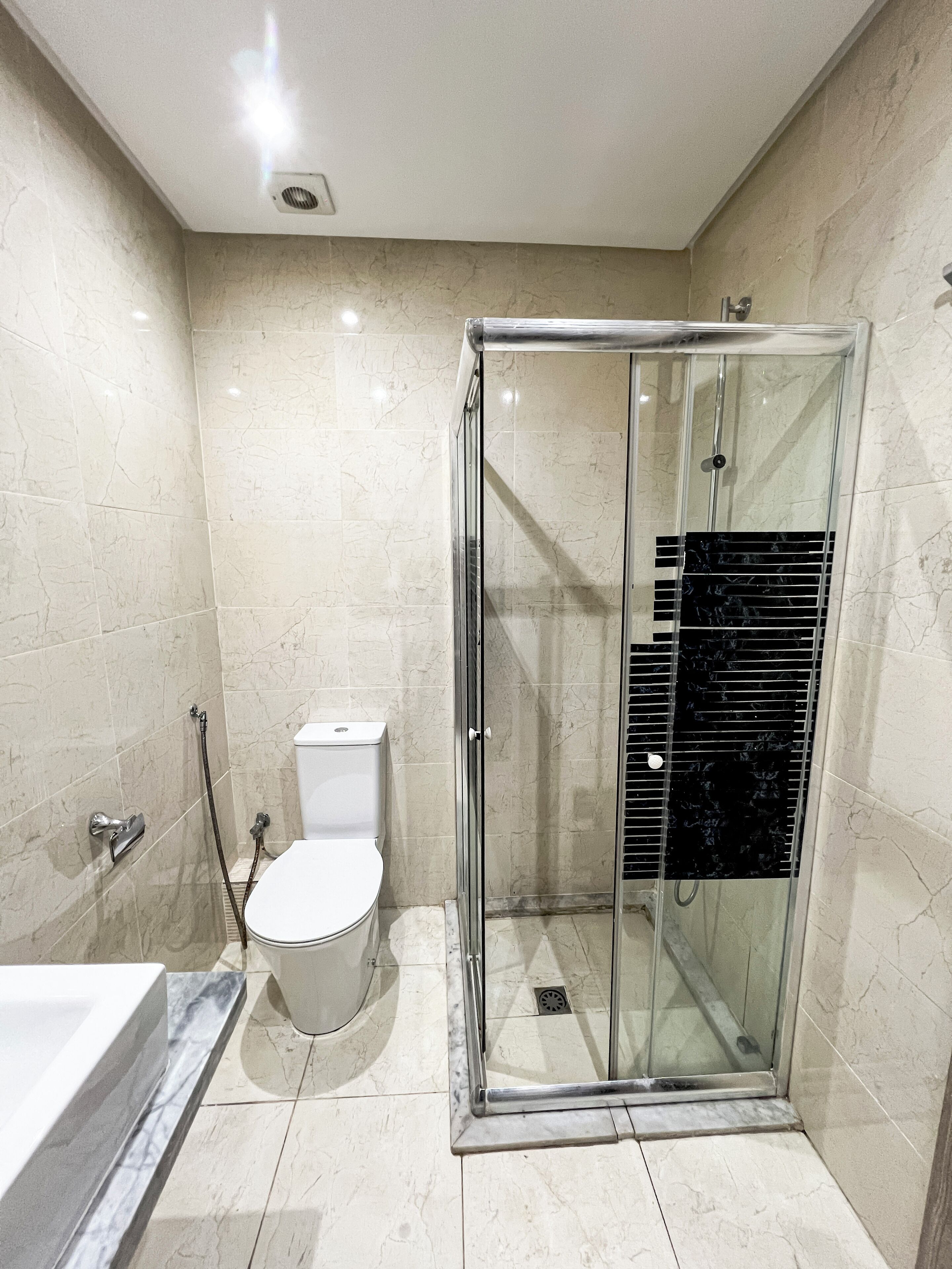 A modern bathroom with a glass-enclosed shower, a white toilet, and a marble-tiled floor.