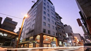 Un hôtel à plusieurs étages, doté d’un design moderne, avec une entrée imposante et un rez-de-chaussée bien visible où se trouvent des boutiques.