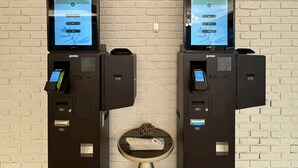 Deux bornes en libre-service, dotées d’écrans, de lecteurs de cartes et d’une petite table placée entre elles, sur laquelle se trouve un vase.