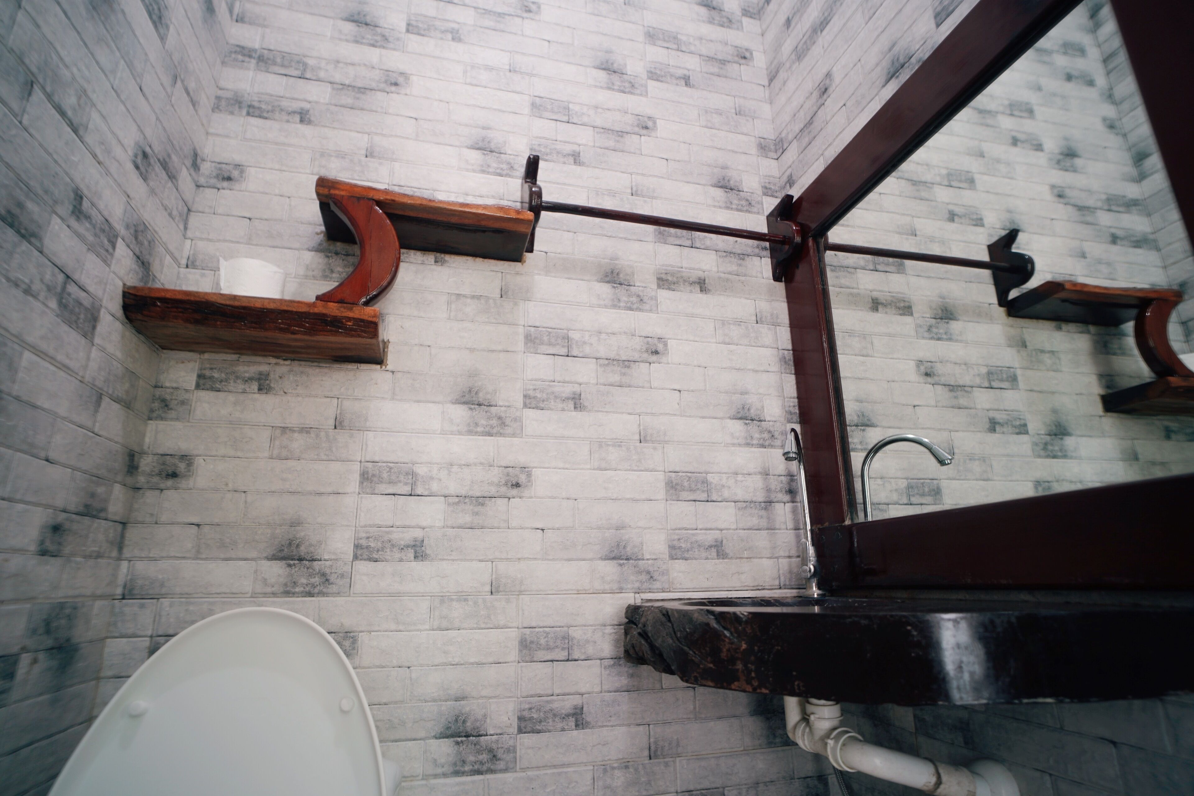 Un baño con inodoro blanco, estante de madera y espejo.