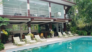 A pool area with lounge chairs and a glass-enclosed building with a balcony. - Ocean 202 Homestay (General Luna)