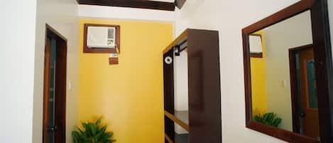 A hallway with yellow walls, a potted plant, a wooden bench, and a mirror on the wall.