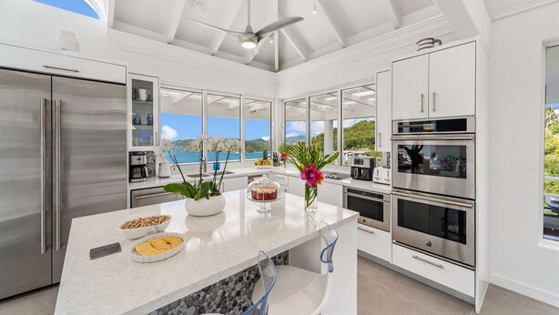 Una cocina moderna con una isla grande, electrodomésticos de acero inoxidable y vista al mar.