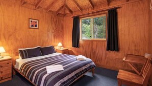 Un dormitorio con paneles de madera, una cama grande, dos mesitas de noche con lámparas, una ventana con cortinas y una silla de madera.