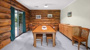 A log cabin interior with a wooden dining table, chairs, and a cabinet.