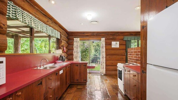 A log cabin kitchen with wooden cabinets, a red countertop, and a view of the outdoors.