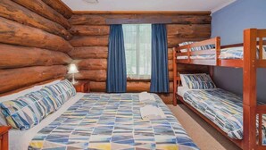 A log cabin room with a large bed, two smaller beds, a nightstand, and a window with curtains.