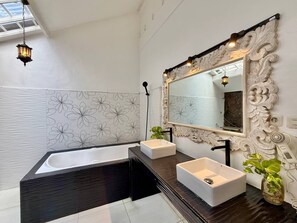 A modern bathroom with a freestanding bathtub, two sinks, and a large mirror with ornate detailing. - Villa White Orchid (Seminyak)