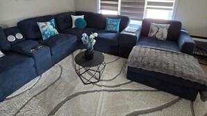 A living room with a dark blue sectional sofa, a round coffee table, and a patterned rug. - Central & Cozy 3BR Home 15 mins to Niagara Falls (St. Catharines)