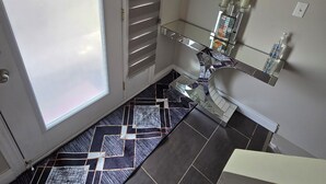 A hotel room with a sliding door, a small glass table with a decorative item, a wall-mounted welcome sign, and a tiled floor. - Central & Cozy 3BR Home 15 mins to Niagara Falls (St. Catharines)