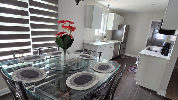 A modern kitchen with a glass dining table, dark floor tiles, and a hanging light fixture. - Central & Cozy 3BR Home 15 mins to Niagara Falls (St. Catharines)