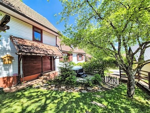 Une maison traditionnelle avec un toit en tuiles, une porte en bois et un petit jardin agrémenté d’un arbre et d’un banc.